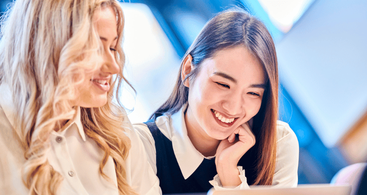 Two female students smiling and looking at a laptop