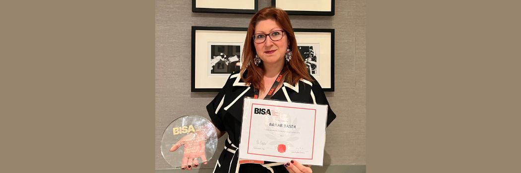 Dr Bahar Baser looking at the camera holding a circular glass award and a certificate