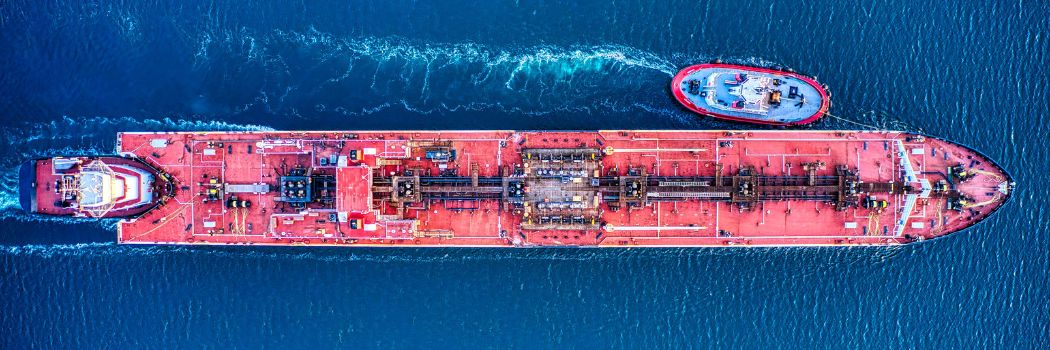 Aerial view of a container ship being guided by tug boats on a blue ocean