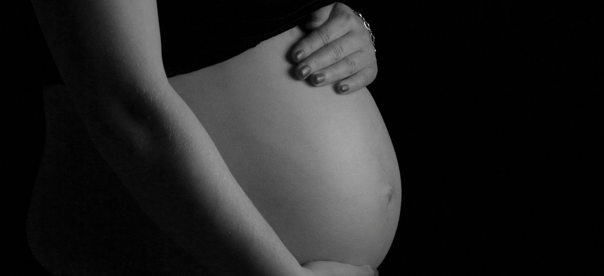 Black and white image showing a pregnant abdomen cradled with a pair of hands