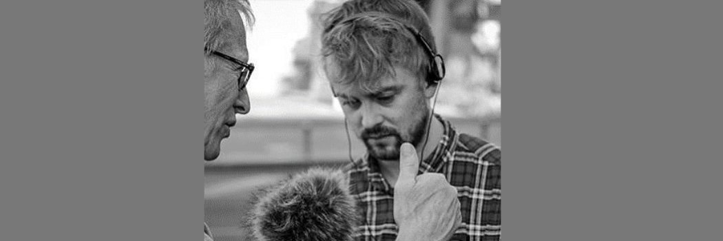 A black and white image of David Knowles holding a microphone looking towards the ground