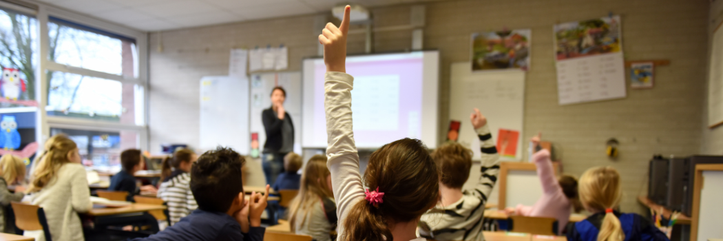 A girl raises her hand next to a boy while learning in a classroom