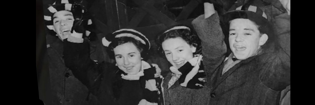 A group of male and female Newcastle United fans wearing black and white scarves and hats