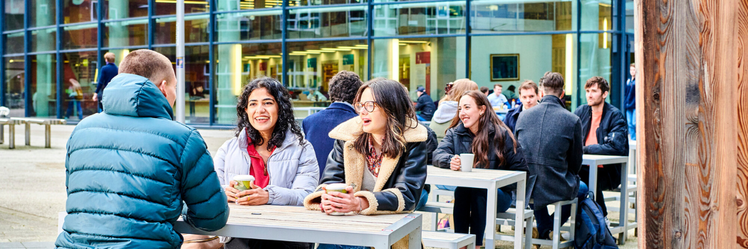 A groups of students chatting on benches outside the library