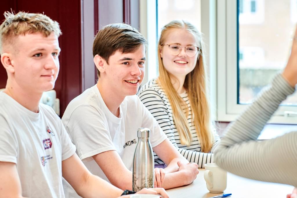 A group of male and female students sit around a long table chatting