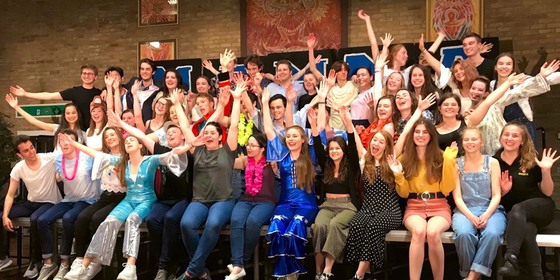 A large group of students sitting on a stage in the theatre space