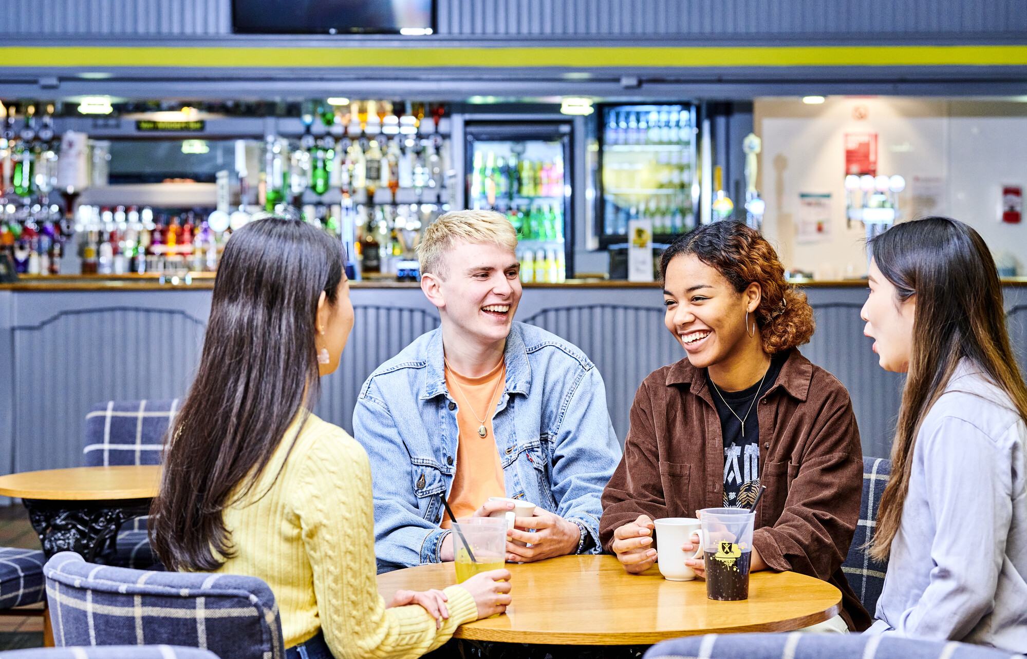 A group of students having a drink while seated around a table while several other students sit and talk at another table