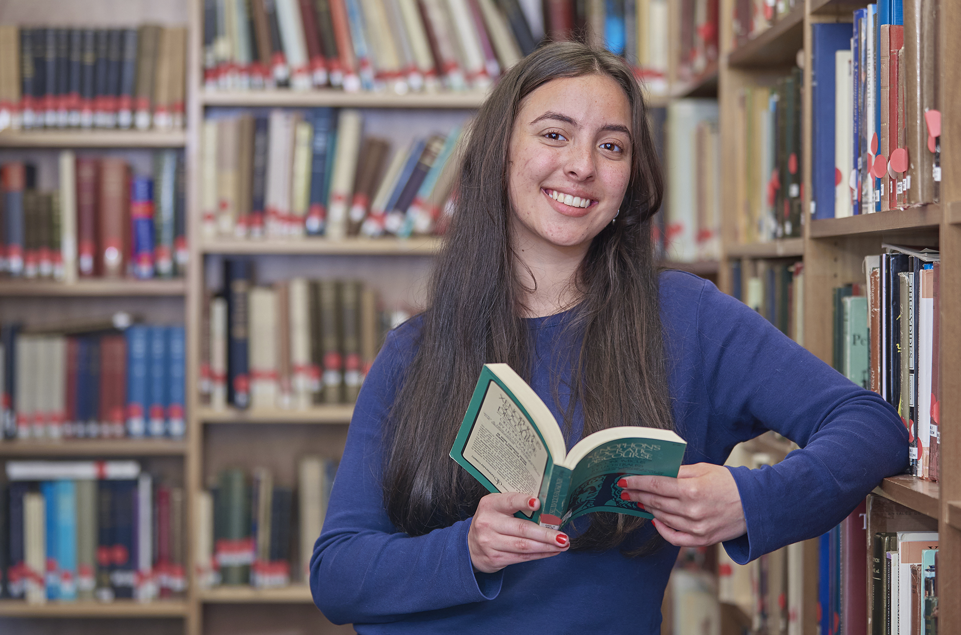 Classics students leaning at shelf of Classics library reading a book