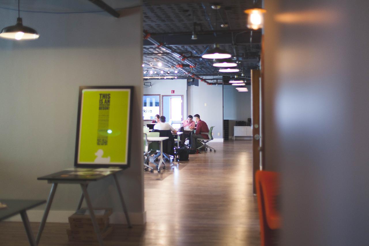 A corridor that ends in a room with a conference table surrounded by a group of people with laptops