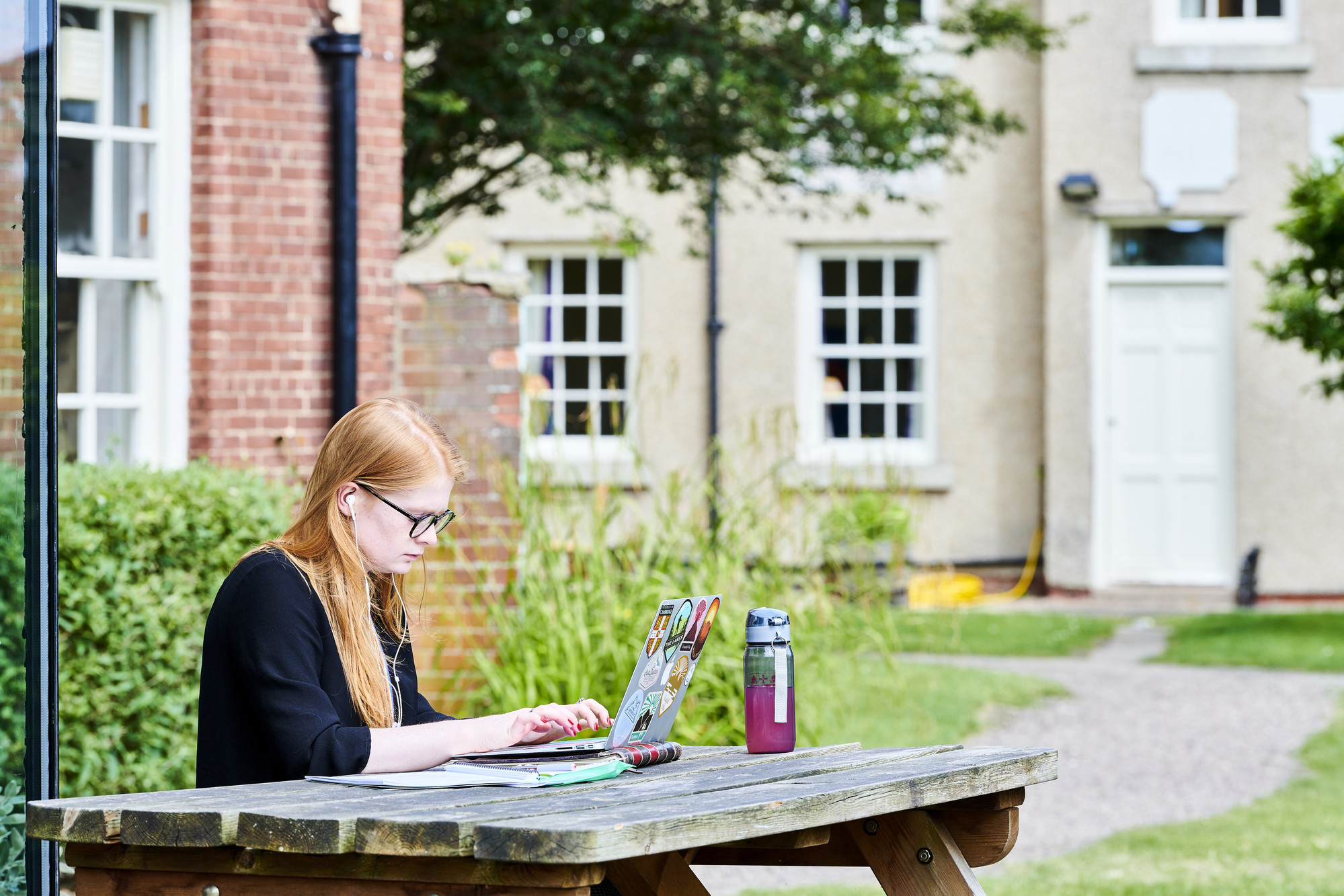 Student working on laptop at bench outside