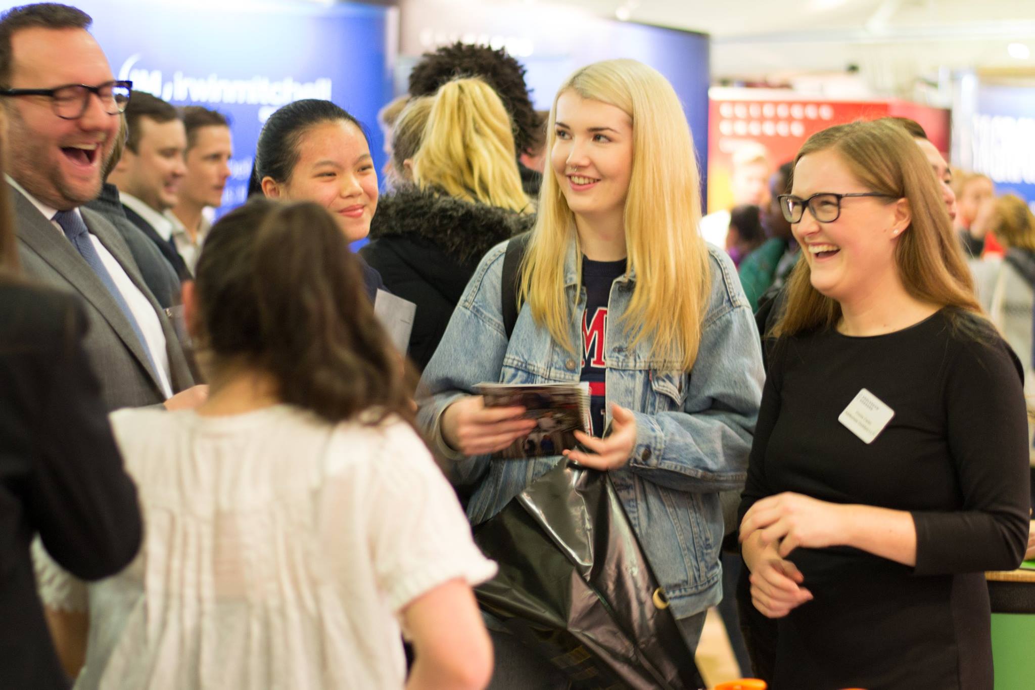 A blonde student smiles at employers while another student to the right laughs.